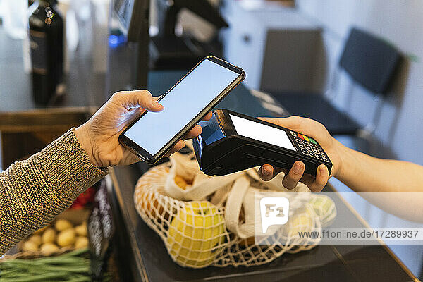 Weibliche Kundin beim Online-Bezahlen mit dem Handy im Supermarkt