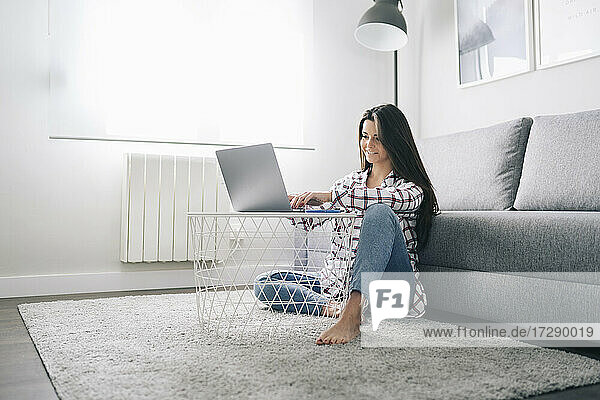 Lächelnde Frau  die im Wohnzimmer sitzend am Laptop arbeitet