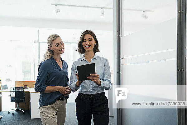 Junge Geschäftsfrau  die mit einer Unternehmerin im Büro über ein digitales Tablet diskutiert
