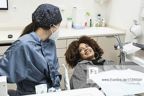 Afro-Patientin lächelt den Zahnarzt mit Gesichtsschutzmaske in der Klinik an
