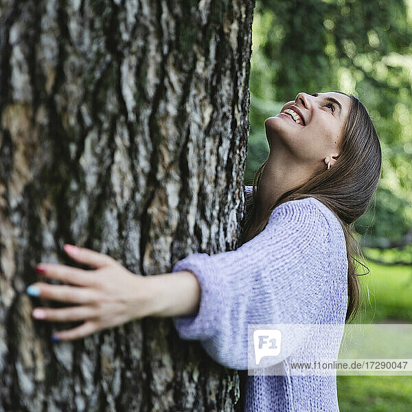 Smiling woman embracing tree in public park