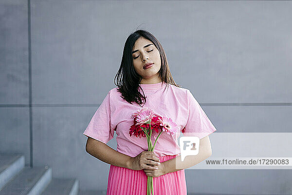Frau mit geschlossenen Augen  die einen Strauß rosa Blumen in der Hand hält