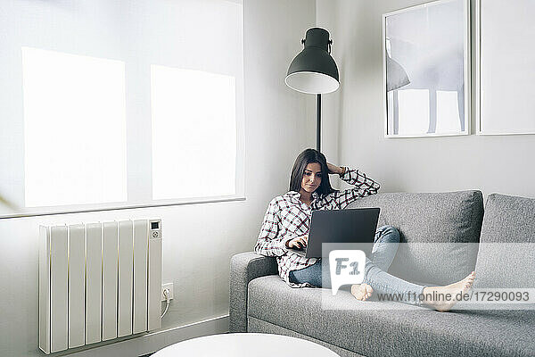 Junge Frau benutzt einen Laptop  während sie sich zu Hause auf dem Sofa ausruht