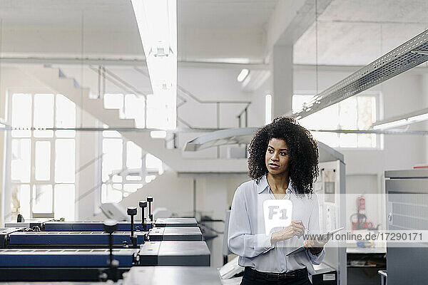 Afro female entrepreneur looking away while working with digital tablet in industry