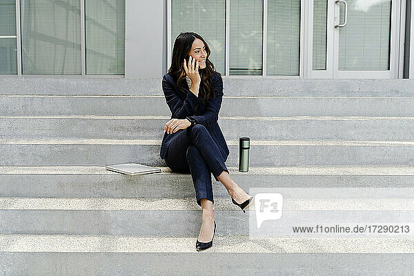 Geschäftsfrau  die auf einer Treppe sitzend mit ihrem Smartphone telefoniert