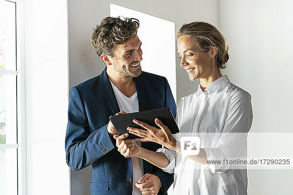Lächelnde Kollegen  die bei der Arbeit im Büro ein digitales Tablet benutzen