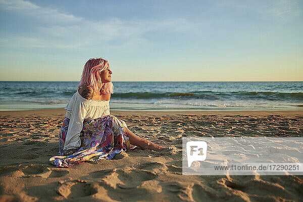 Junge Frau sitzt nachdenklich im Sand am Strand