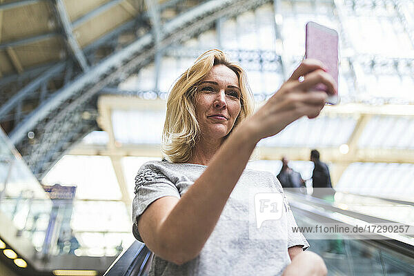 Mature woman taking selfie while moving down on escalator