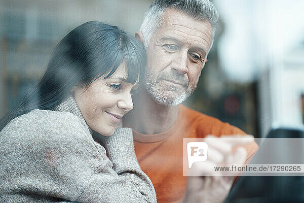 Lächelnde Frau lehnt sich an die Schulter eines Mannes und benutzt ein digitales Tablet in einem Café