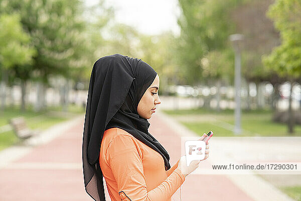 Arabische Frau mit Kopftuch benutzt ein Smartphone in einem öffentlichen Park