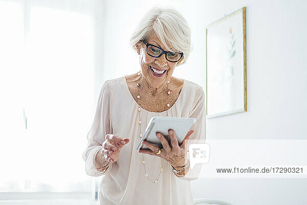 Lächelnde ältere Frau  die zu Hause ein digitales Tablet benutzt