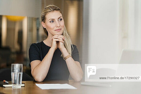 Thoughtful female professional sitting with hand on chin at desk while looking away