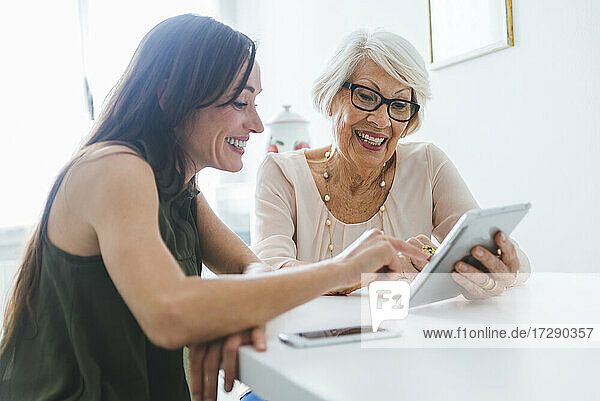 Lächelnde ältere Frau  die ihr digitales Tablet mit ihrer Enkelin zu Hause teilt