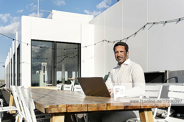 Businessman with laptop sitting at table on office terrace