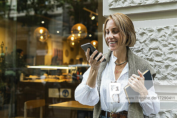 Lächelnde Frau  die ein Mobiltelefon benutzt  während sie vor einer Wand steht