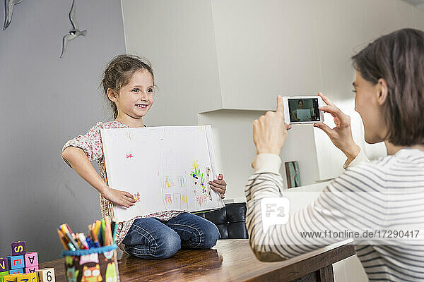 Mutter fotografiert Mädchen mit Gemälde mit dem Handy zu Hause