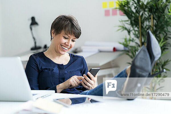Lächelnde weibliche Fachkraft  die im Büro mit ihrem Handy im Internet surft
