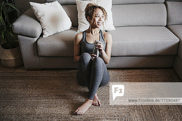 Smiling young woman sitting on carpet in front of sofa at home