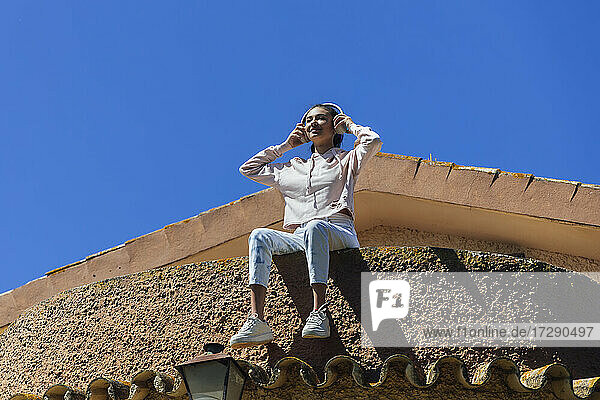 Lächelnde junge Frau  die auf dem Dach sitzend Musik hört