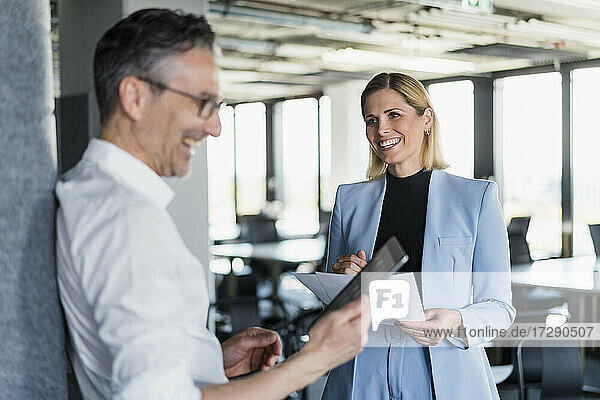 Lächelnde Unternehmerin  die einen männlichen Kollegen bei der Nutzung eines digitalen Tablets im Büro beobachtet