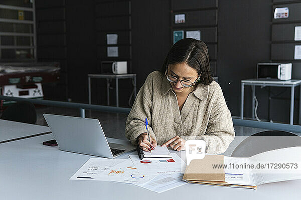 Female professional wearing eyeglasses writing on diary at office