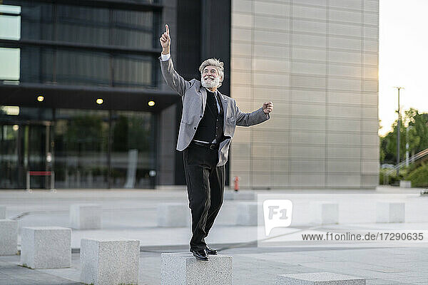 Fröhlicher Geschäftsmann tanzt auf Betonblock bei Bürogebäude