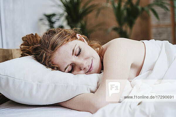 Hemdlose Frau mit Decke auf dem Bett liegend zu Hause