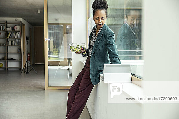 Businesswoman with bowl of salad using digital tablet at office