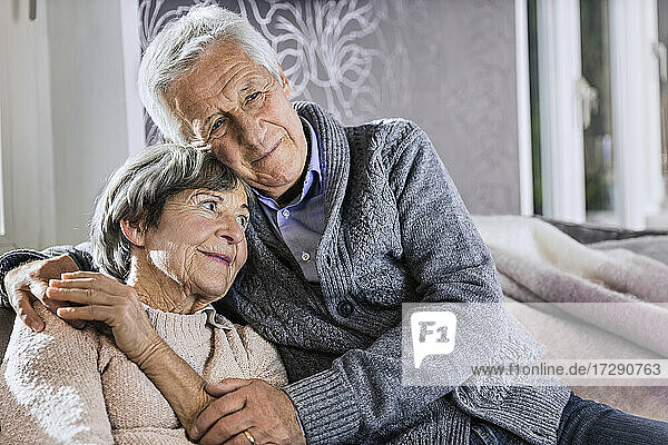 Senior man sitting with arm around on woman in living room