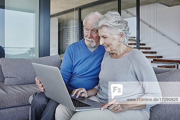 Surprised man looking at laptop used by woman while sitting in living room