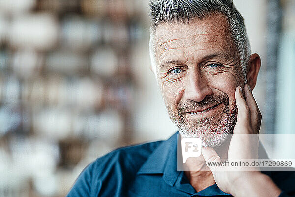 Männlicher Besitzer mit Hand am Kinn lächelnd in einem Café