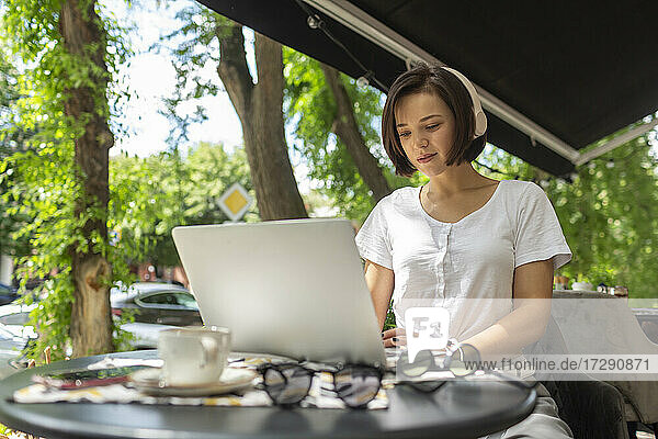 Junge Berufstätige  die einen Laptop benutzen und über Kopfhörer Musik hören  in einem Café sitzend