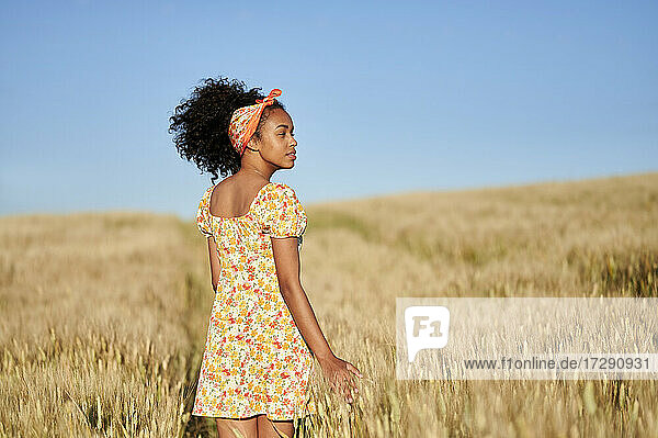 Junge Frau mit lockigem Haar  die in einem Weizenfeld steht und wegschaut