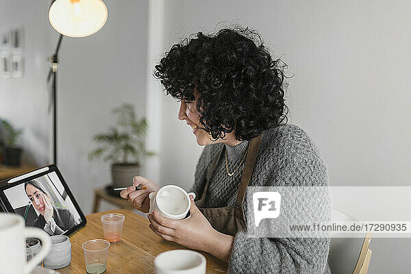 Lächelnde Künstlerin mit Tasse  die in einem Workshop mit einem digitalen Tablet lernt