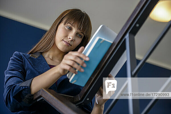 Junge Geschäftsfrau  die ein digitales Tablet benutzt  während sie auf einer Treppe im Büro steht