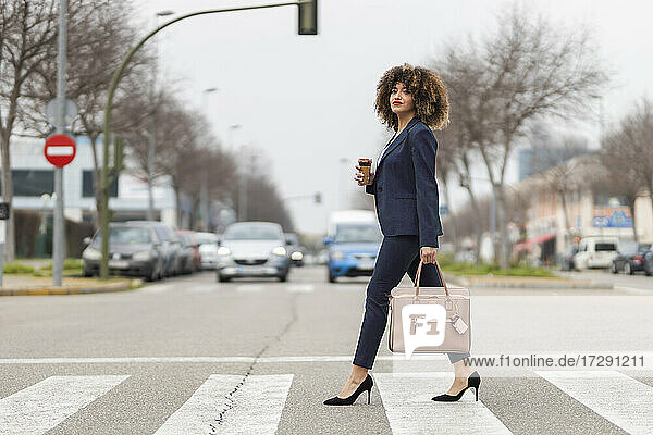 Gut gekleidete Geschäftsfrau mit Handtasche beim Überqueren der Straße in der Stadt