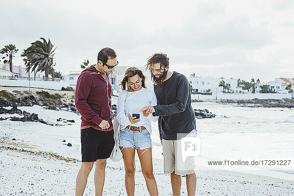 Freunde  die am Strand stehen und ein Mobiltelefon benutzen