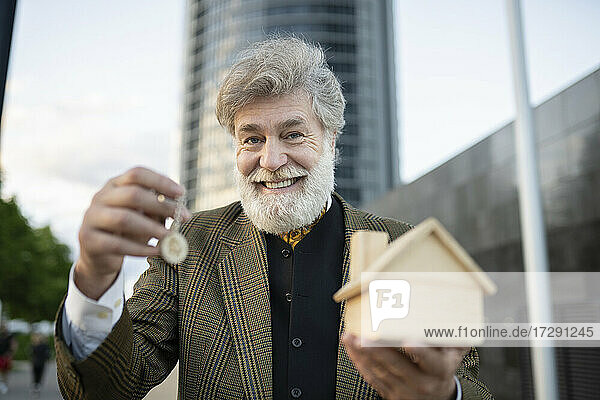 Lächelnder männlicher Immobilienmakler  der ein Musterhaus und einen Schlüssel in der Stadt anbietet