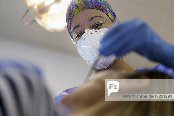 Zahnärztin mit Gesichtsschutzmaske bei der Untersuchung der Zähne eines Patienten in einer Klinik