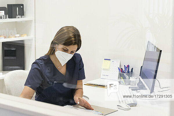 Zahnärztin mit Gesichtsschutzmaske bei der Arbeit am Schreibtisch in einer Klinik