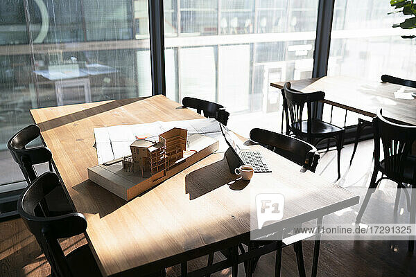Architekturmodell und Bauplan mit Laptop auf einem Tisch in einer Büro-Cafeteria