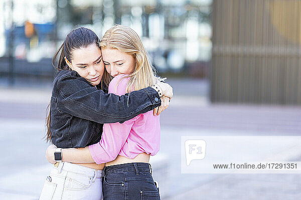 Beautiful female friends hugging in city