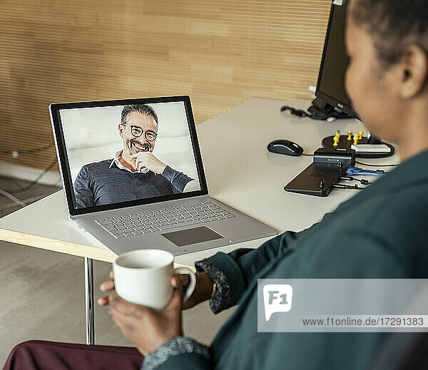 Geschäftsfrau mit Kaffeetasse während einer Videokonferenz über einen Laptop am Schreibtisch