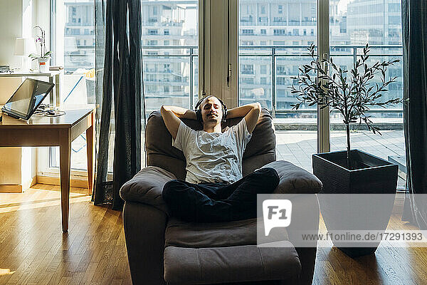Junger Mann mit Händen hinter dem Kopf  der sich auf einem Liegestuhl zu Hause entspannt