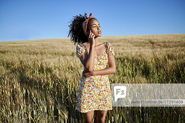 Junge Frau in einem Kleid  die in einem Weizenfeld steht und wegschaut