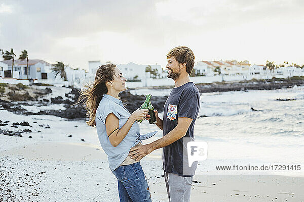 Mittleres erwachsenes Paar stößt auf Getränke an  während sie am Strand stehen