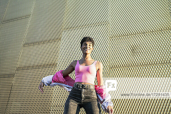 Lächelnde junge Frau an einer Mauer an einem sonnigen Tag