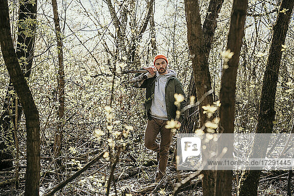 Man carrying wood on shoulder amidst bare trees in forest