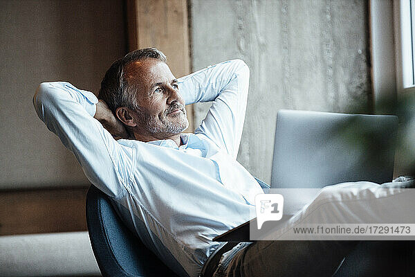 Thoughtful businessman looking away while sitting with laptop in office