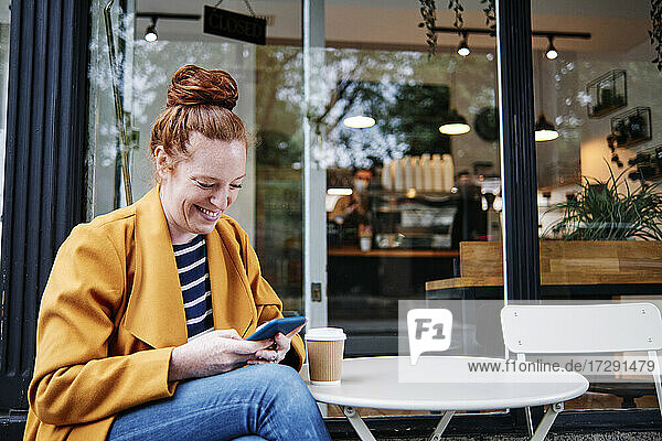 Lächelnde Frau  die ein Smartphone benutzt  während sie in einem Café sitzt